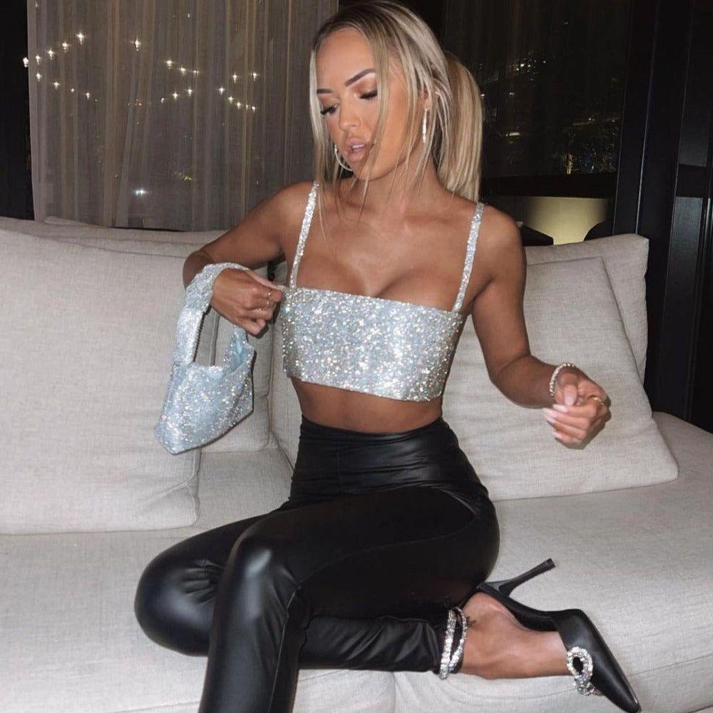 A woman in silver sparkly top and black leather pants is sitting on a couch.