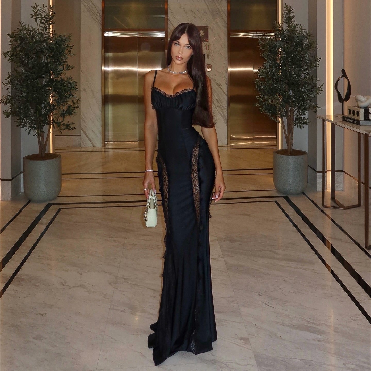 Woman in a black dress standing in a luxurious interior setting with marble floors and gold accents.
