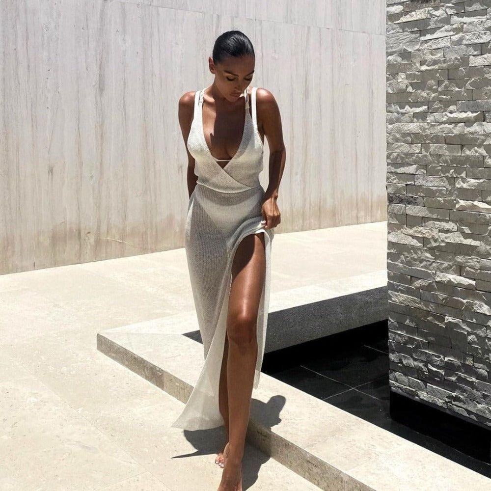 Woman in a white dress with a high slit standing outdoors near a stone wall.