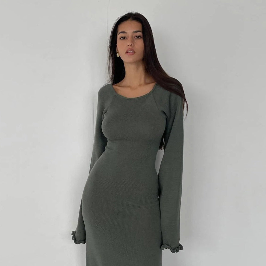 Woman wearing a long-sleeve green dress against a plain background