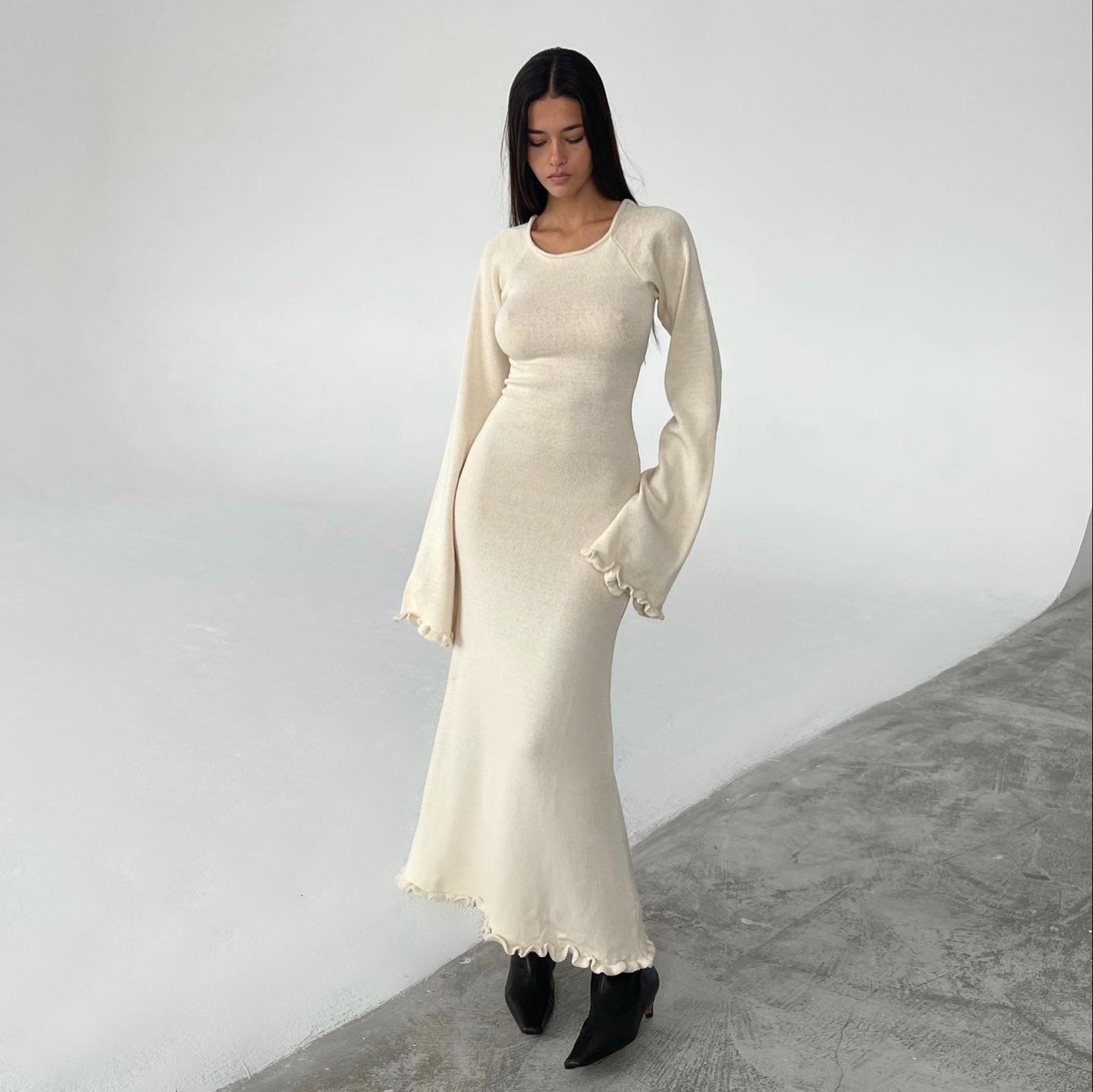 Woman wearing a long, white dress with a fitted bodice and flared sleeves against a plain background.