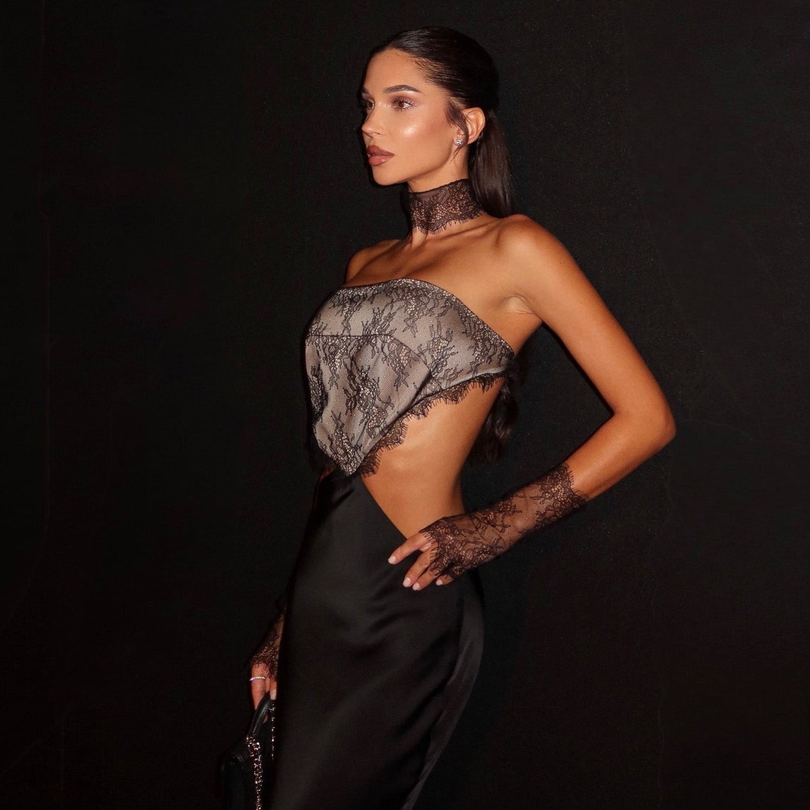 Woman wearing a black and gray lace top with a black skirt against a dark background