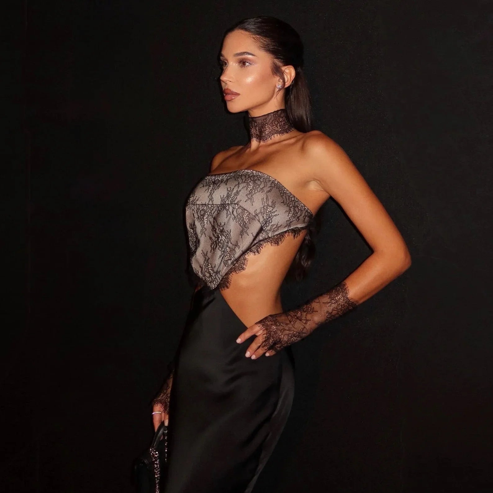 Woman wearing a black and gray lace top with a black skirt against a dark background