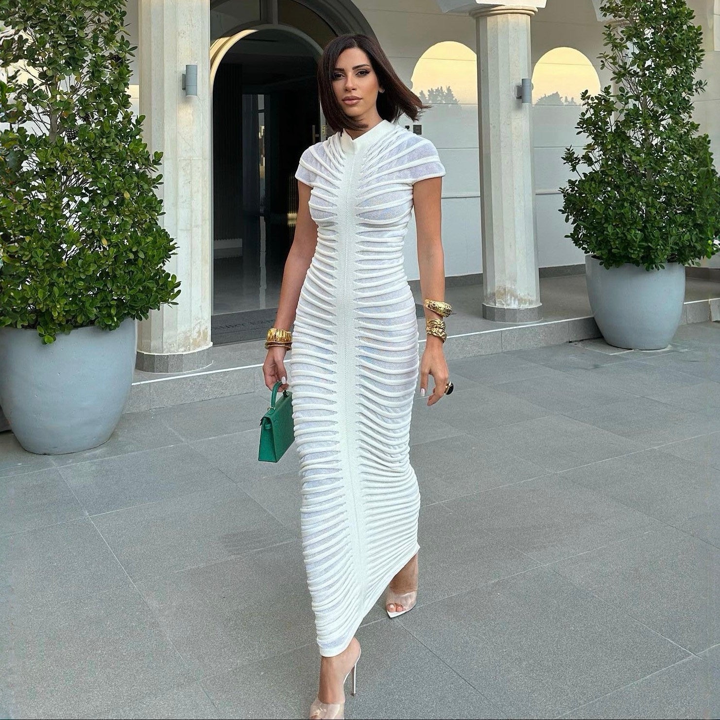 Woman in a white dress standing in front of a building with columns and plants.