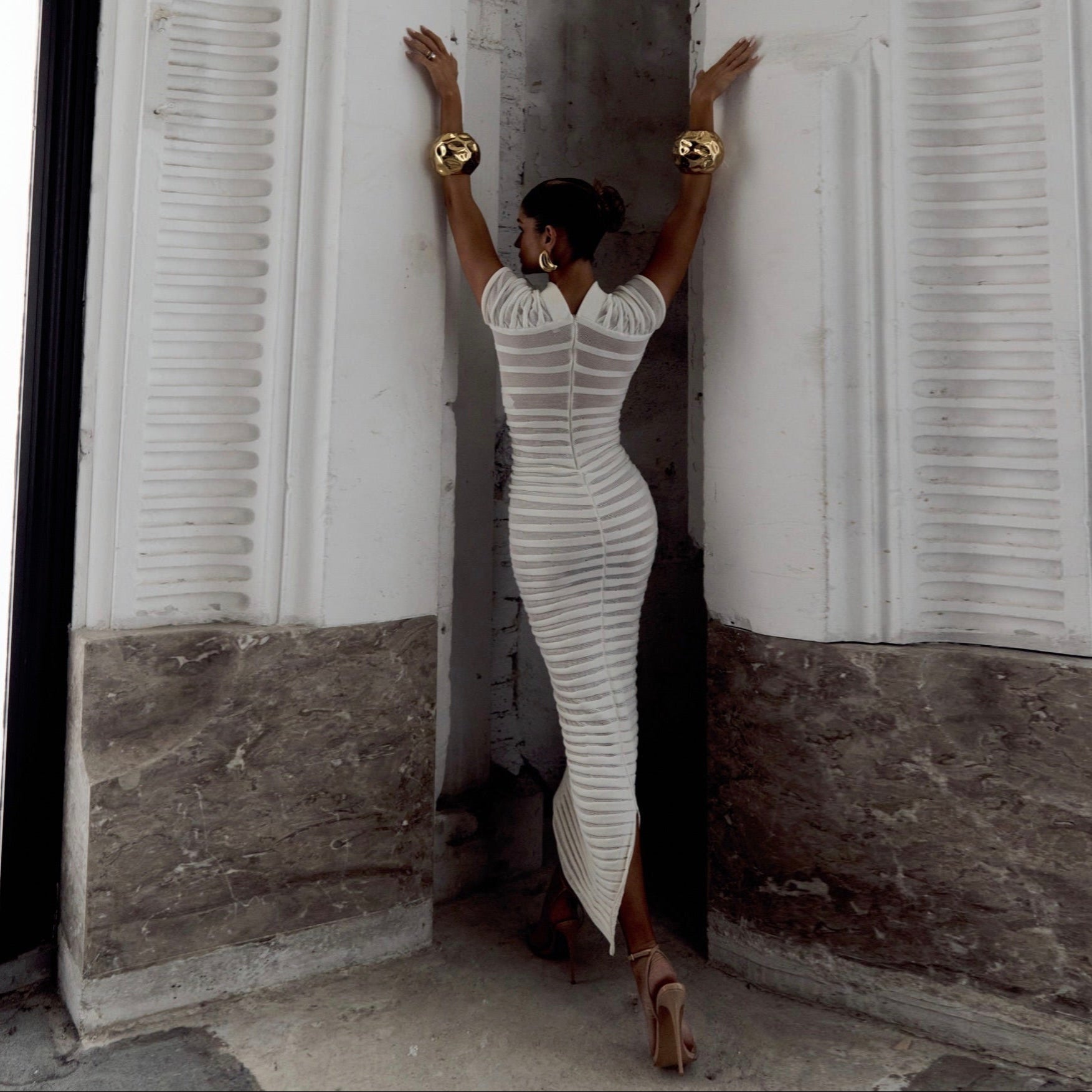 Woman in a white dress standing against a textured wall.