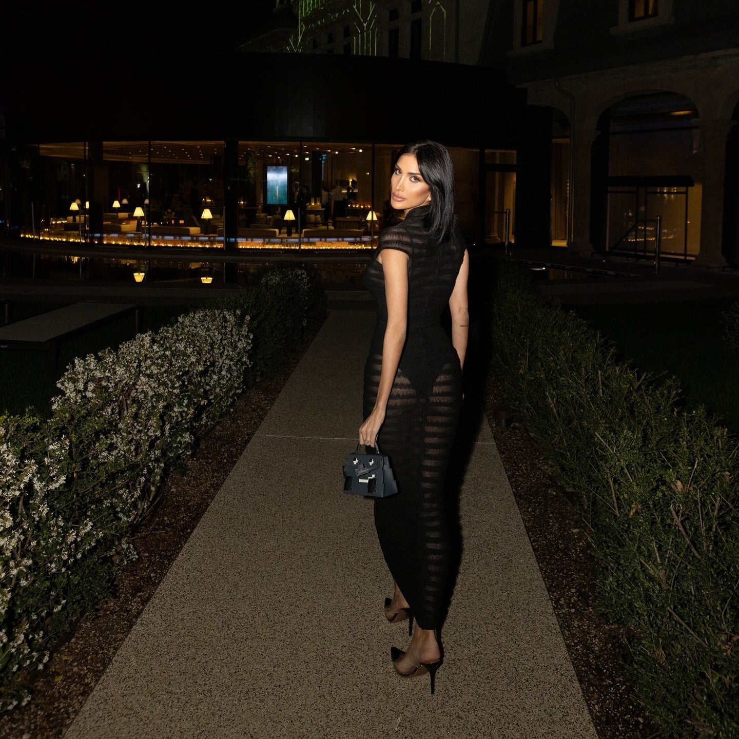Woman in a black dress walking on a path at night with a building in the background