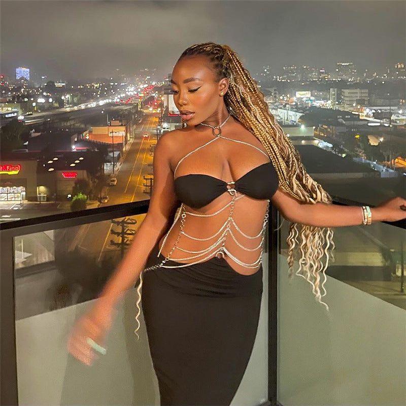 Woman in a black dress with chain details on a balcony at night with city lights in the background