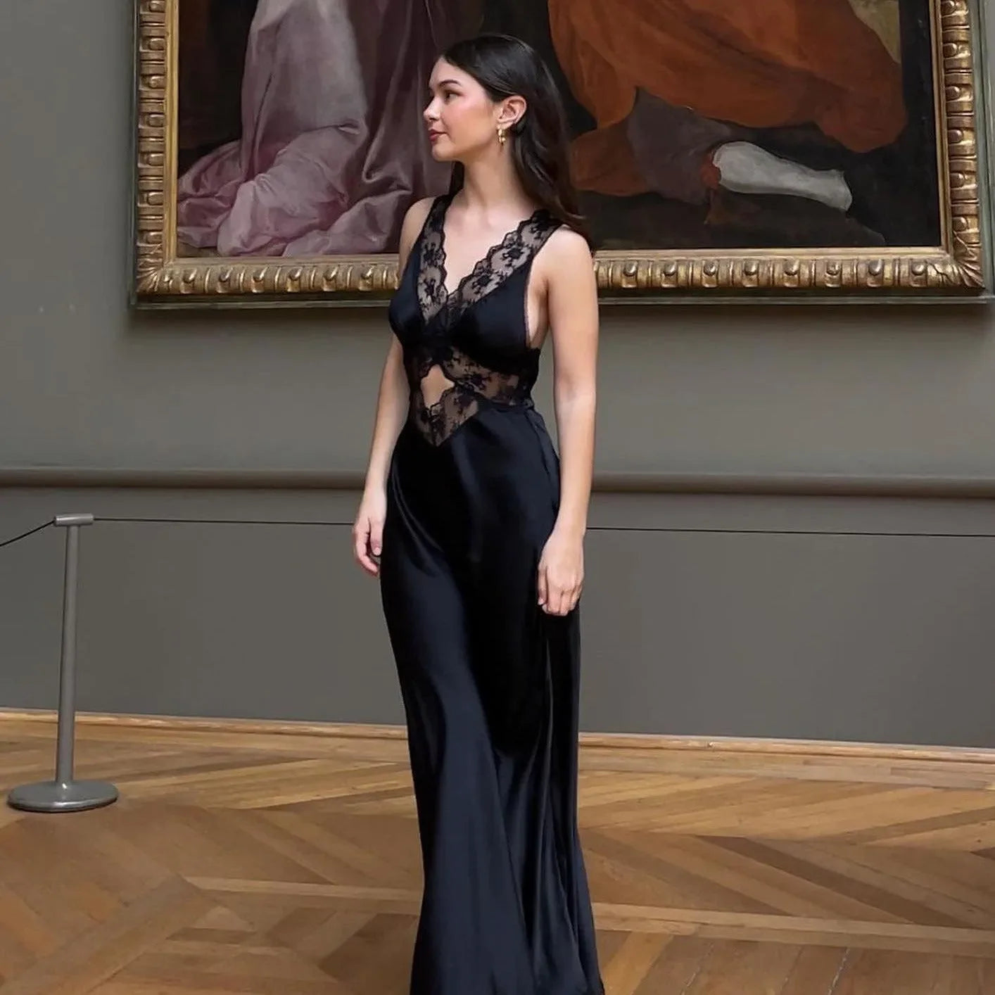 Black satin maxi dress with lace detailing, featuring a plunging neckline, elegantly worn for formal occasions.