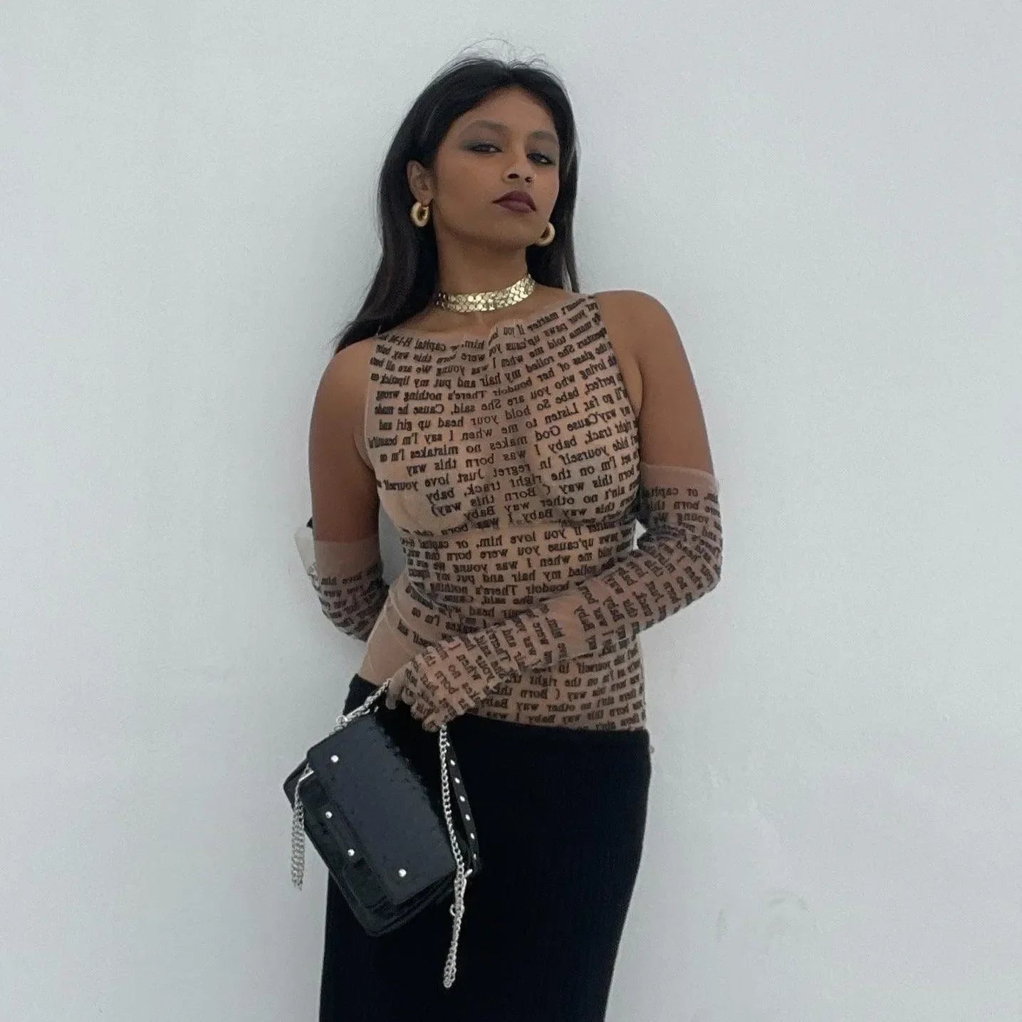 Mesh long-sleeve top with text print and matching gloves, paired with a black clutch, evening look.