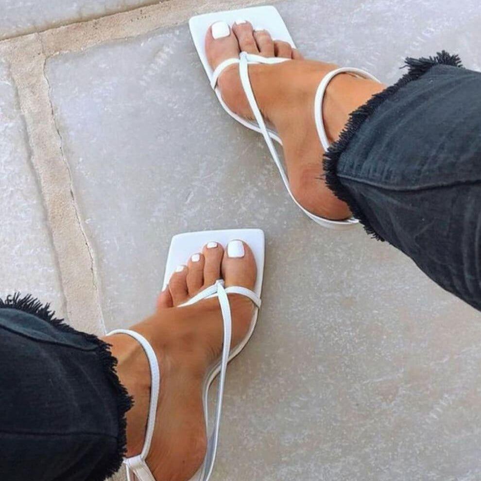 White sandals worn on feet with a neutral background