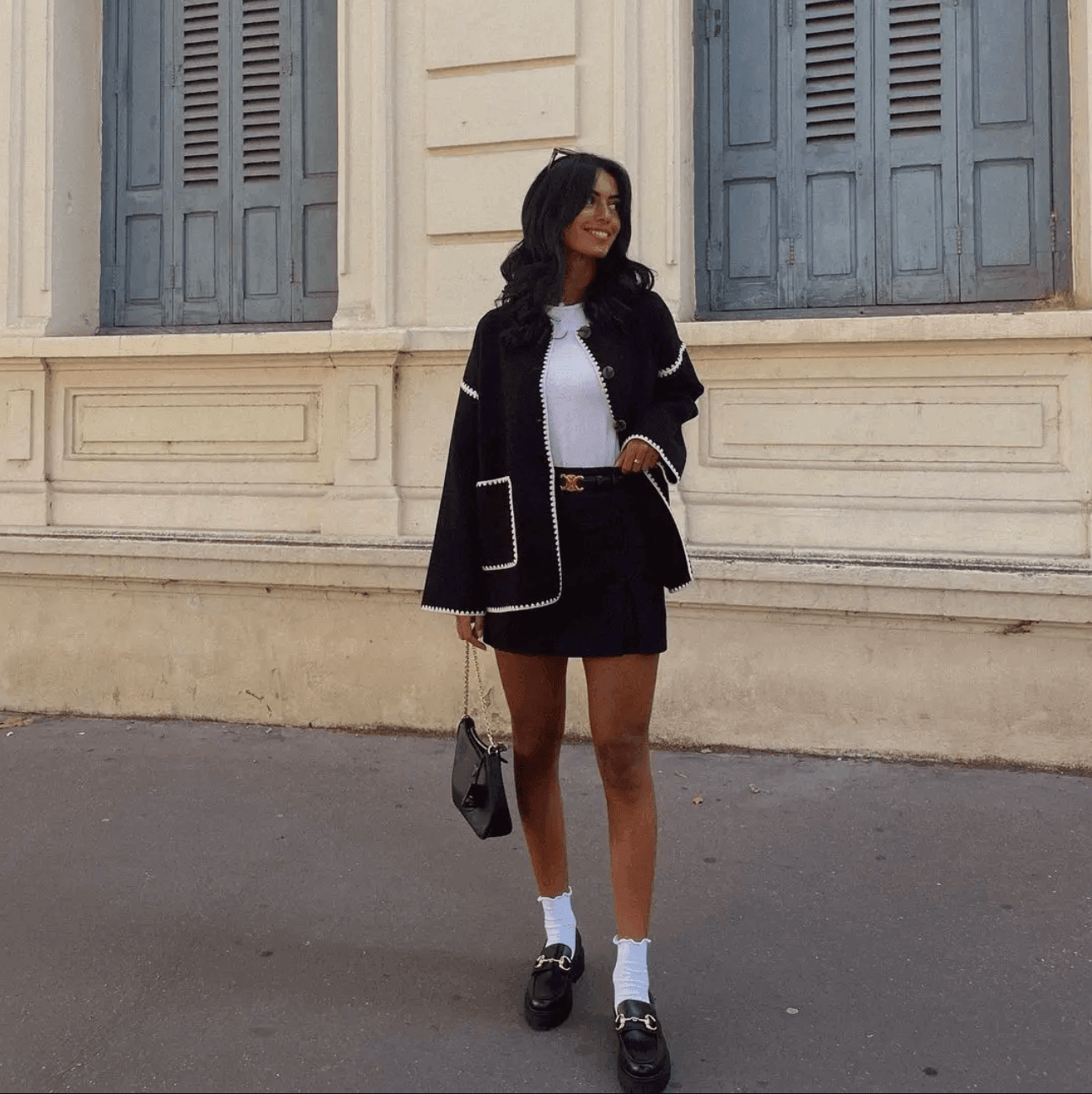 Black mini skirt with belted waist, paired with a white top and a black open-front cardigan, casual