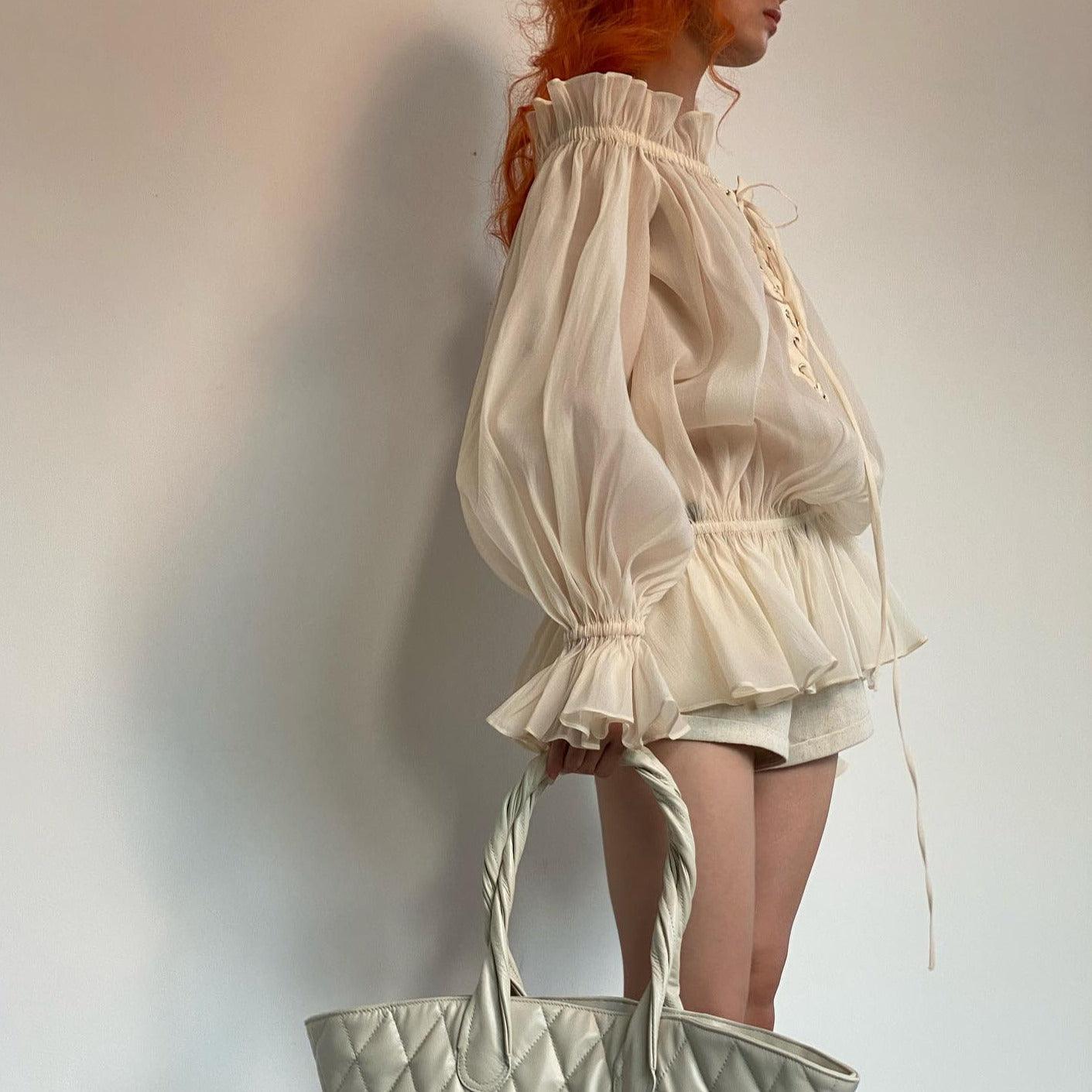 Sheer long-sleeve blouse with ruffled collar and cuff details, paired with a quilted oversized tote