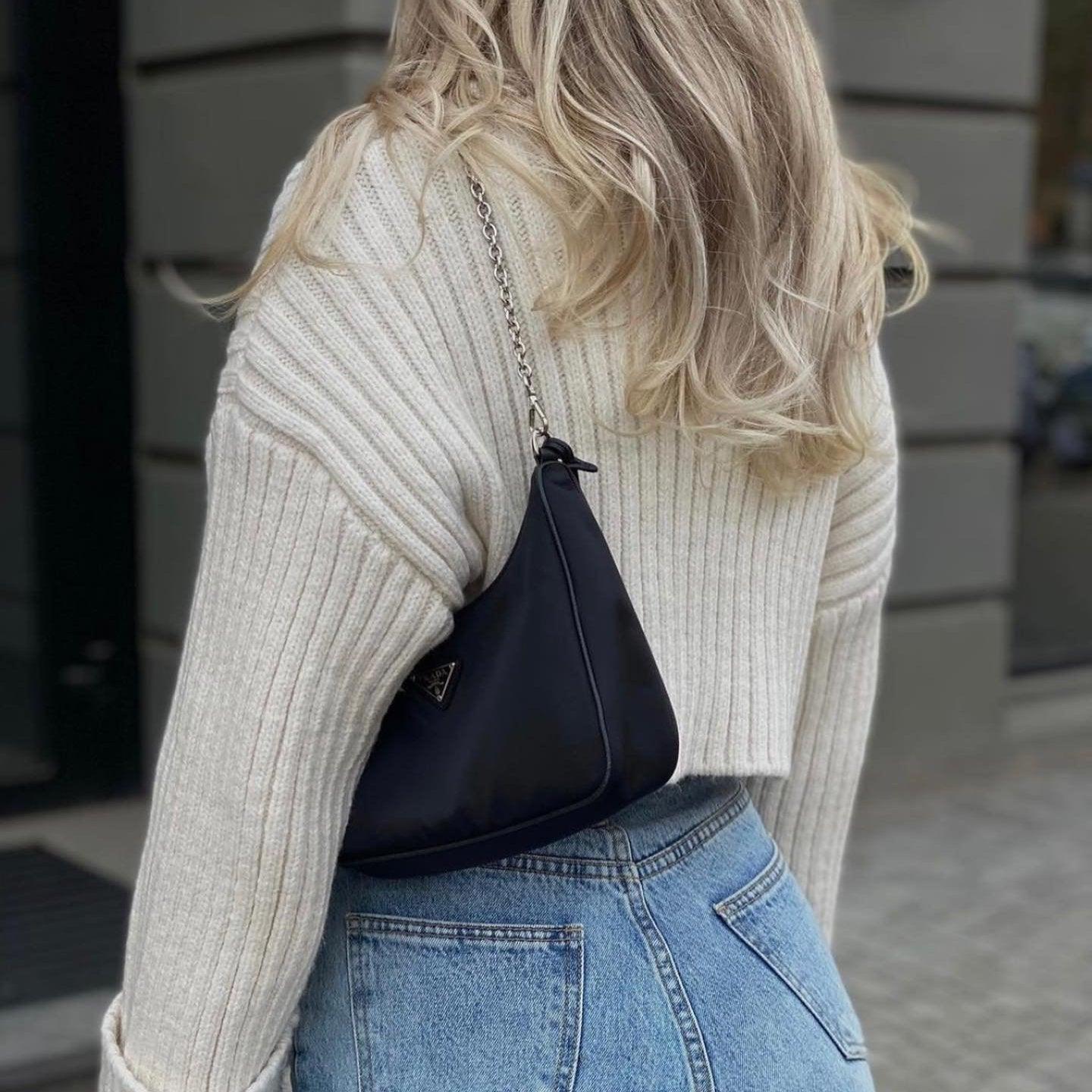 Loose white knitted sweater with ribbed texture, styled with high-waisted denim and a chic black handbag.