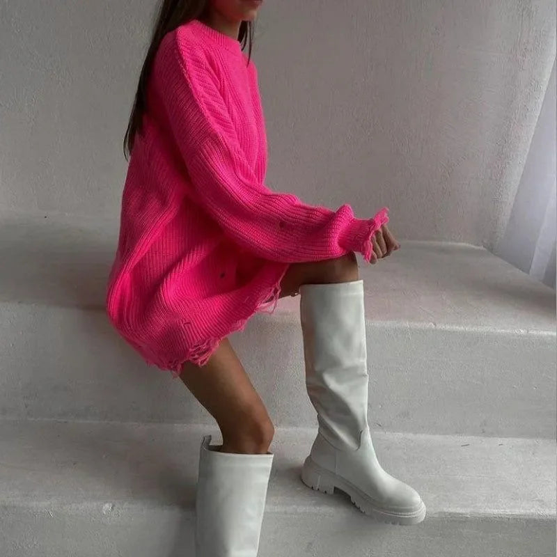 Hot pink loose sweater with broken ribbing detail, styled with knee-high white boots for a trendy look.