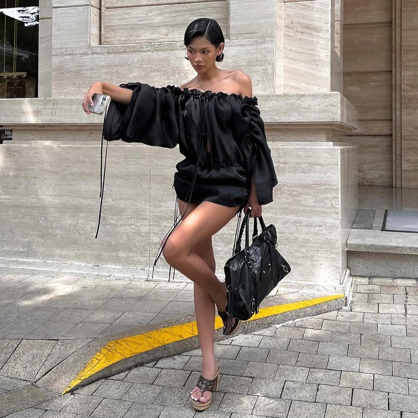 Off-the-shoulder black mini dress with oversized sleeves for evening wear.
