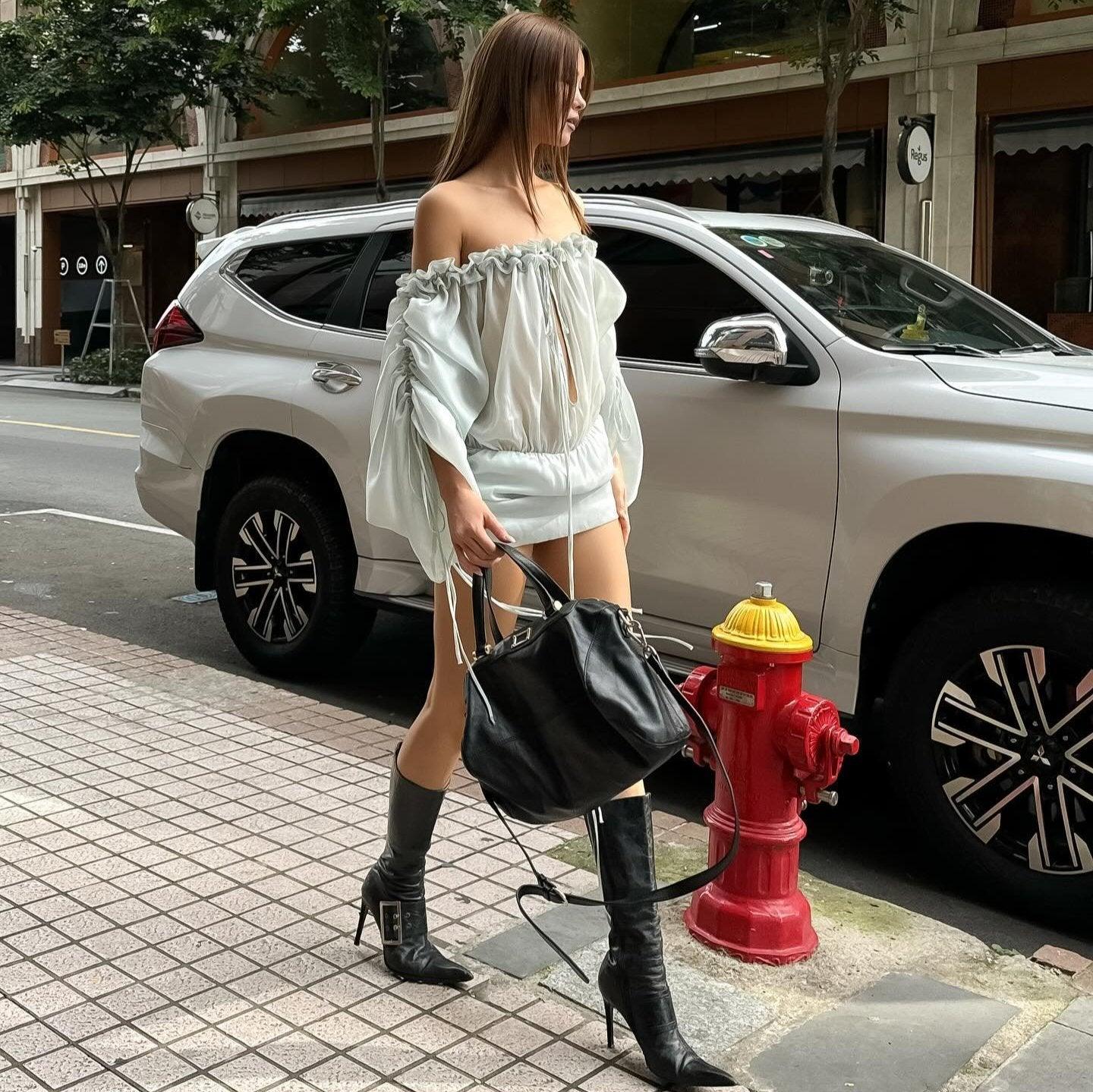 Light blue off-the-shoulder mini dress with cinched waist, styled with knee-high black boots and a black tote.