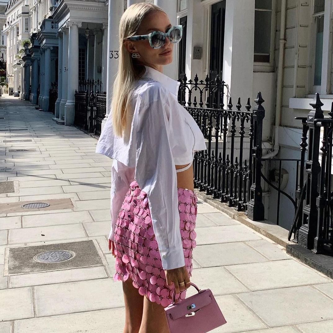 Pink sequin mini skirt with scalloped hem, styled with a cropped white shirt and chic accessories. Perfect for a stylish...