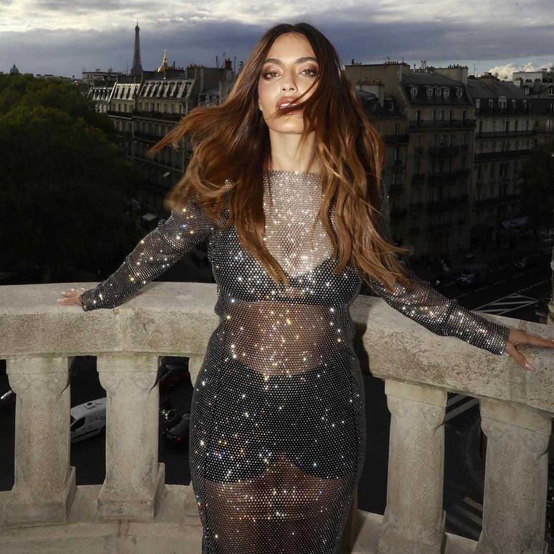 Black rhinestone maxi dress with a fitted silhouette, sheer detailing, styled with long hair flowing against a Parisian...