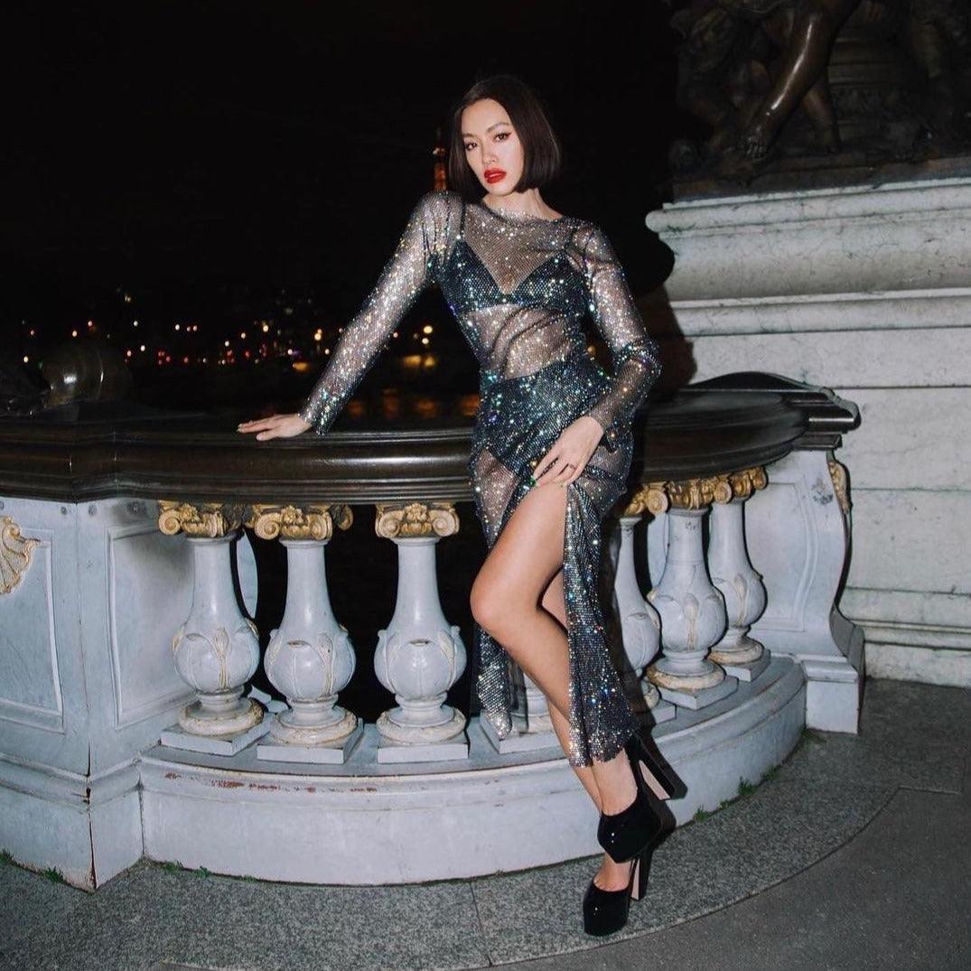 Black rhinestone maxi dress with sheer mesh panels and thigh-high slit, styled with platform heels for a glamorous look.