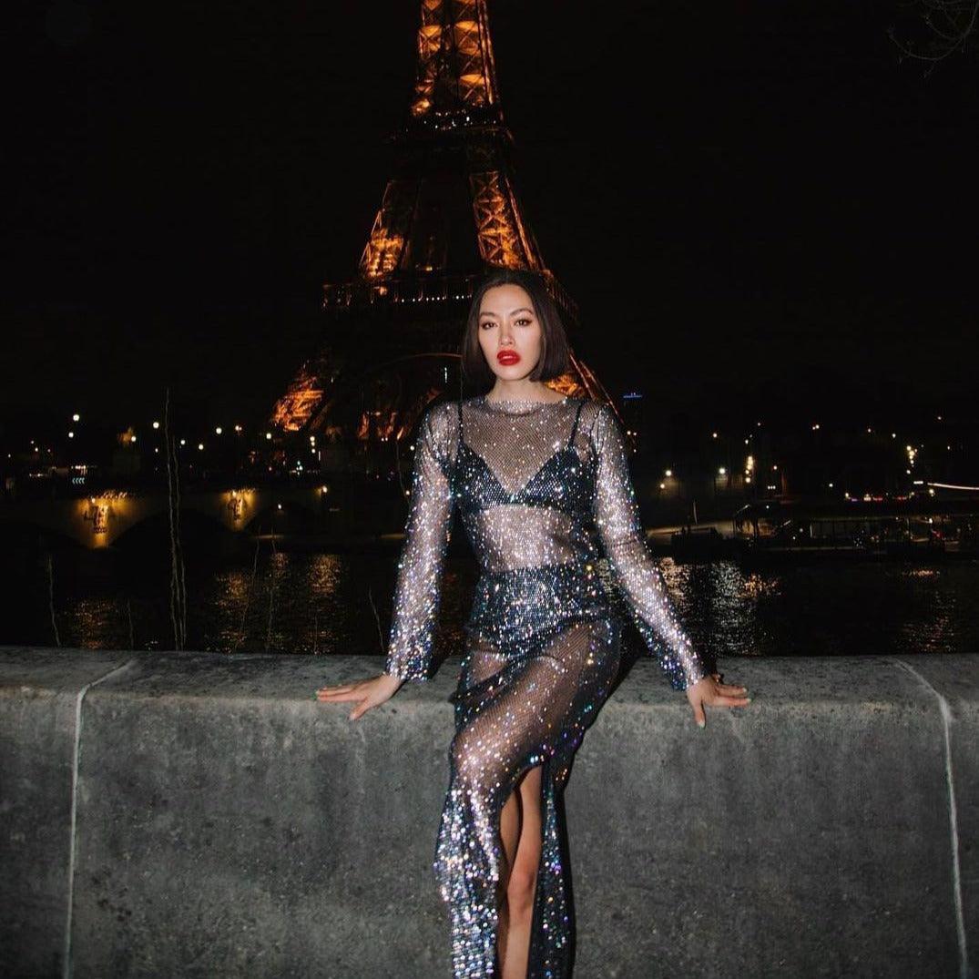 Black maxi dress with rhinestones, featuring a thigh-high slit and sheer long sleeves, styled for an elegant night out.