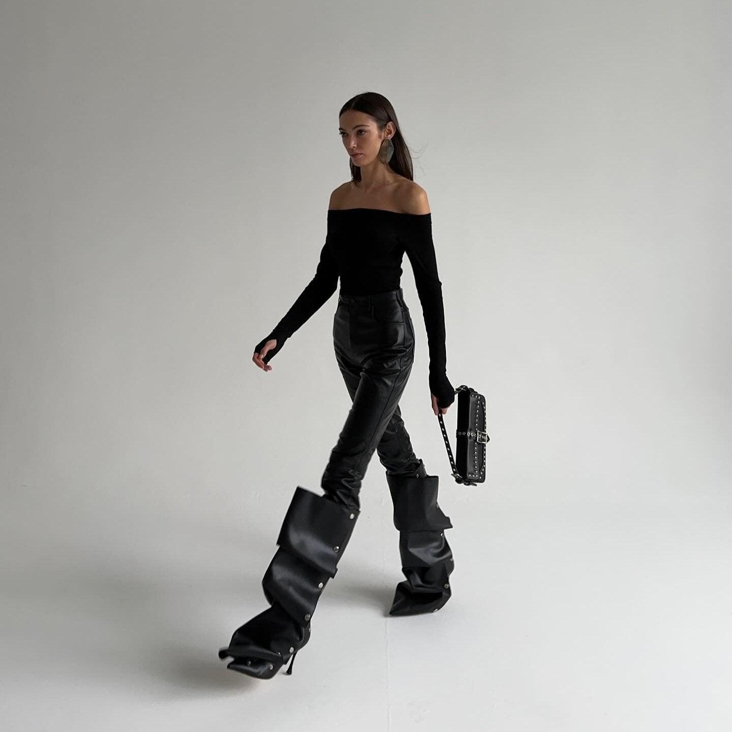 Off-shoulder black top with leather pants, oversized buckle boots, and studded handbag, edgy