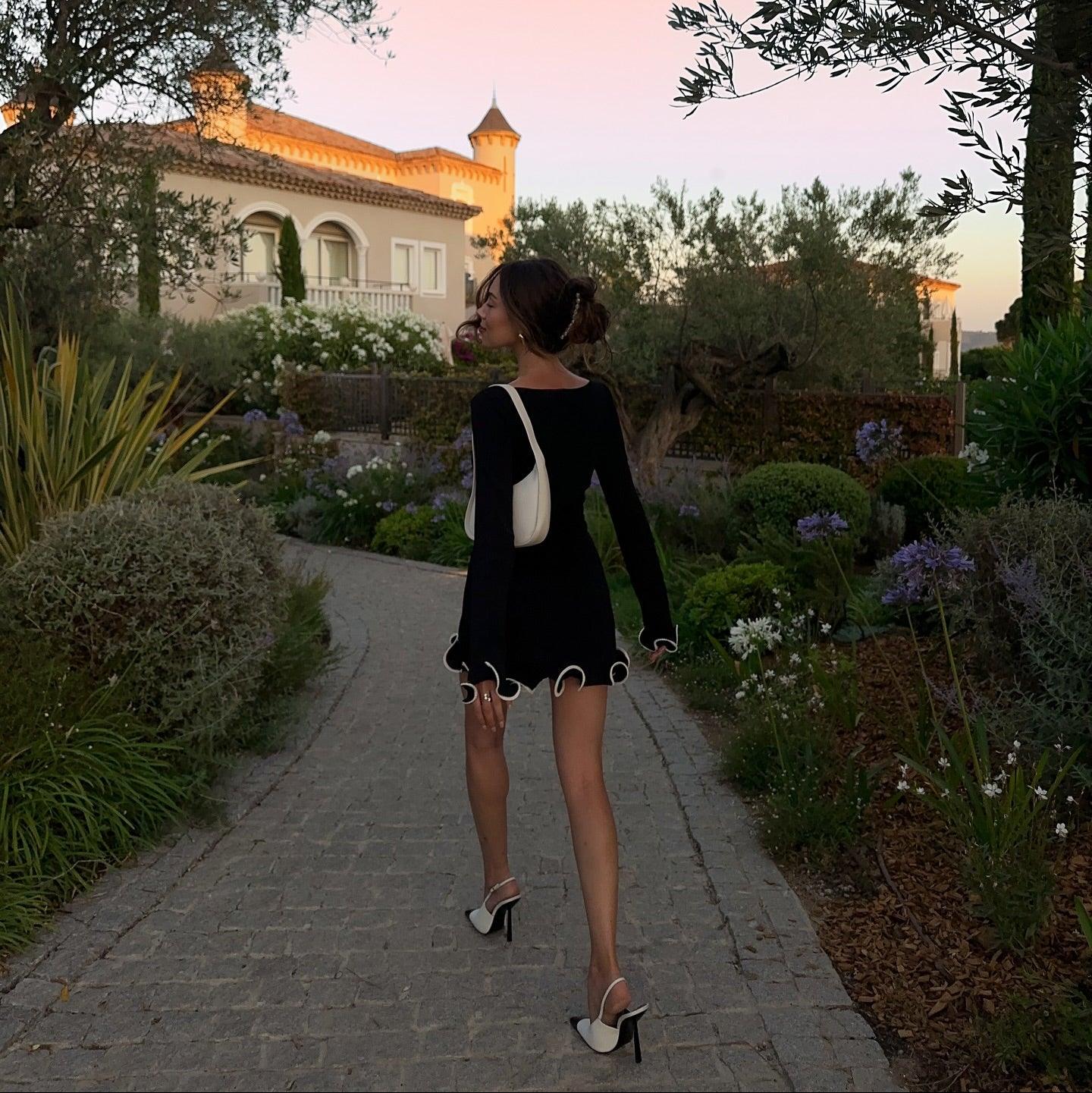 Long-sleeve black mini dress with scalloped hem, paired with white shoulder bag and black-and-white