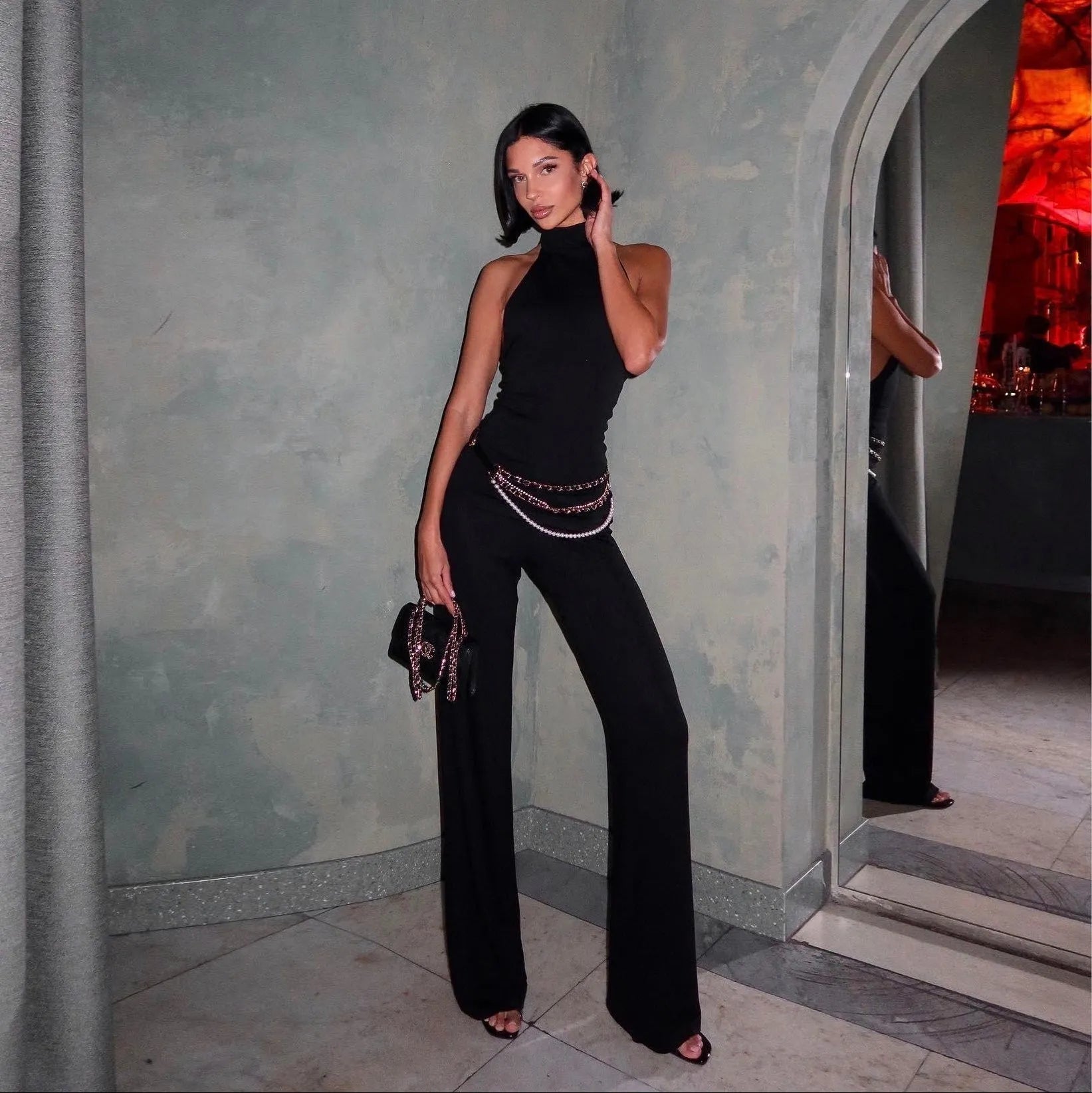 Sleeveless black halter top with wide-leg trousers, accessorized with chain details, sleek evening
