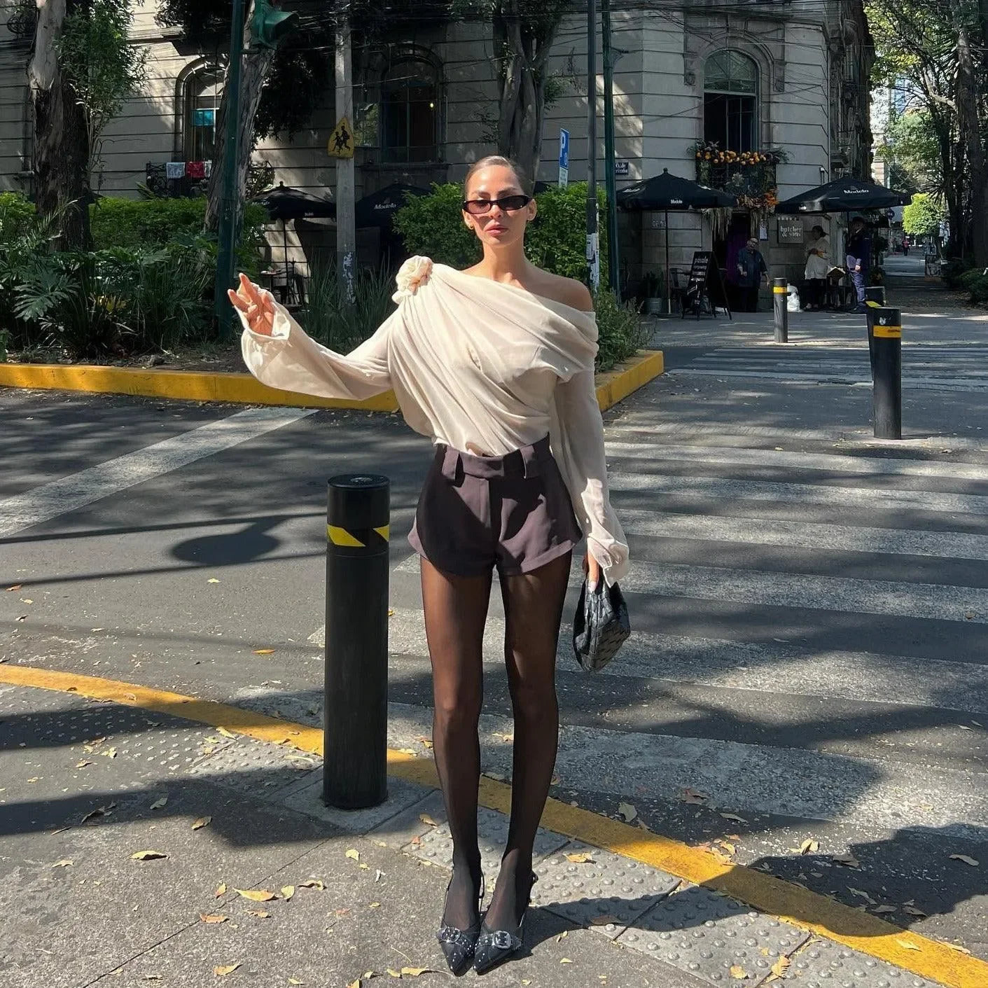 Cream one-shoulder ruched top with black high-waisted shorts, chic day-out style.