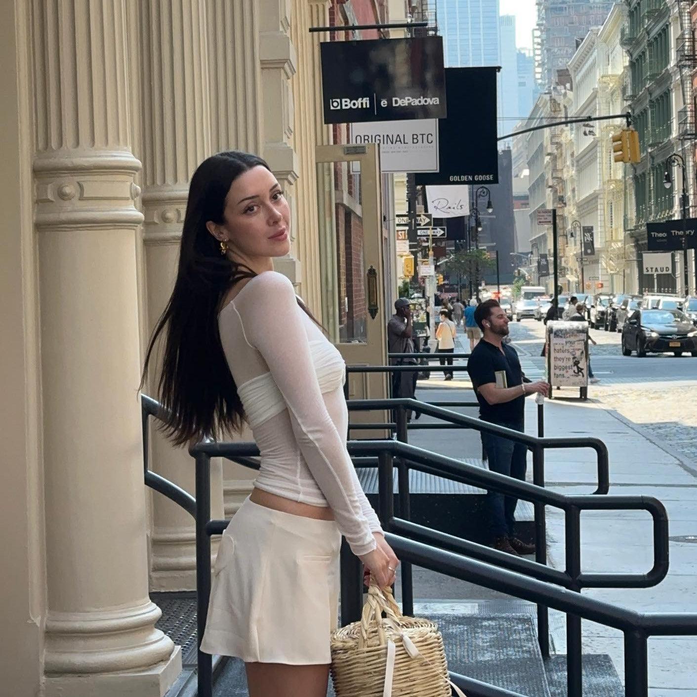 Sheer white long-sleeve top with white mini skirt, casual day look with straw handbag.