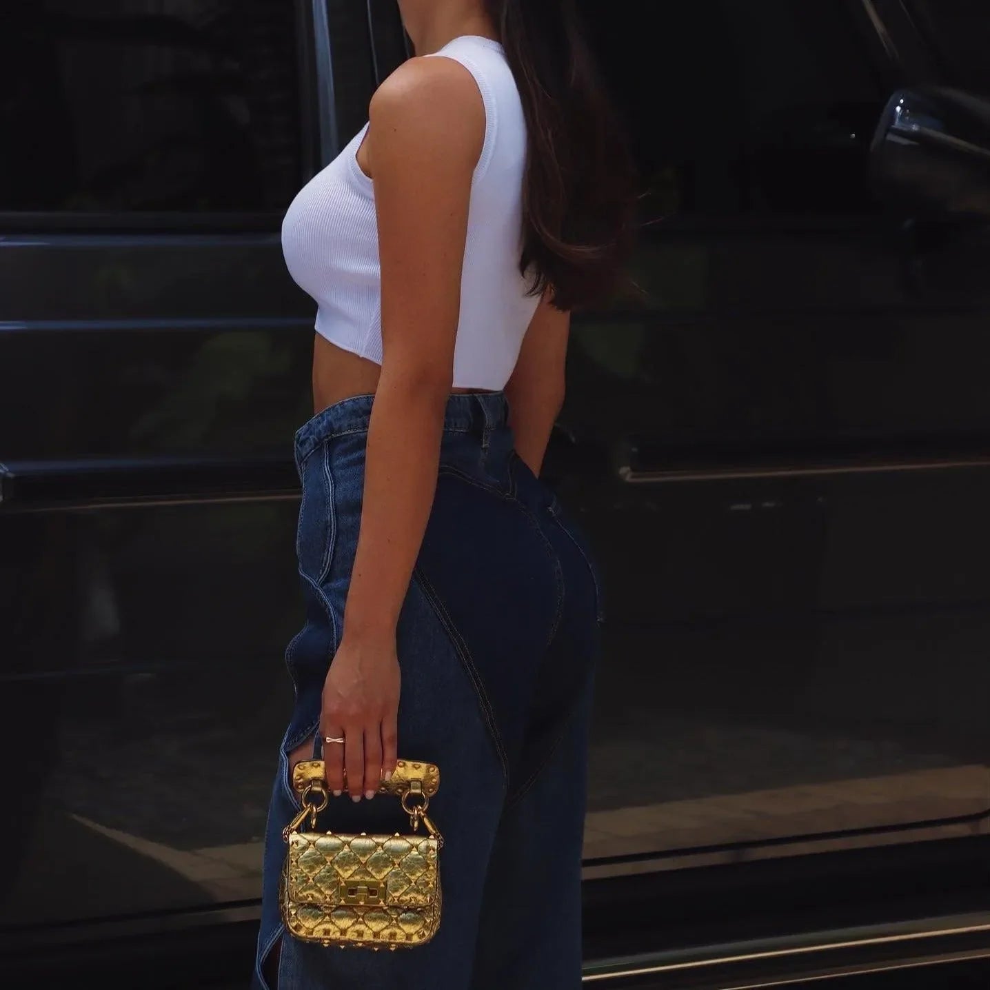 White ribbed crop top and high-waisted denim jeans with a gold quilted handbag, casual street style.