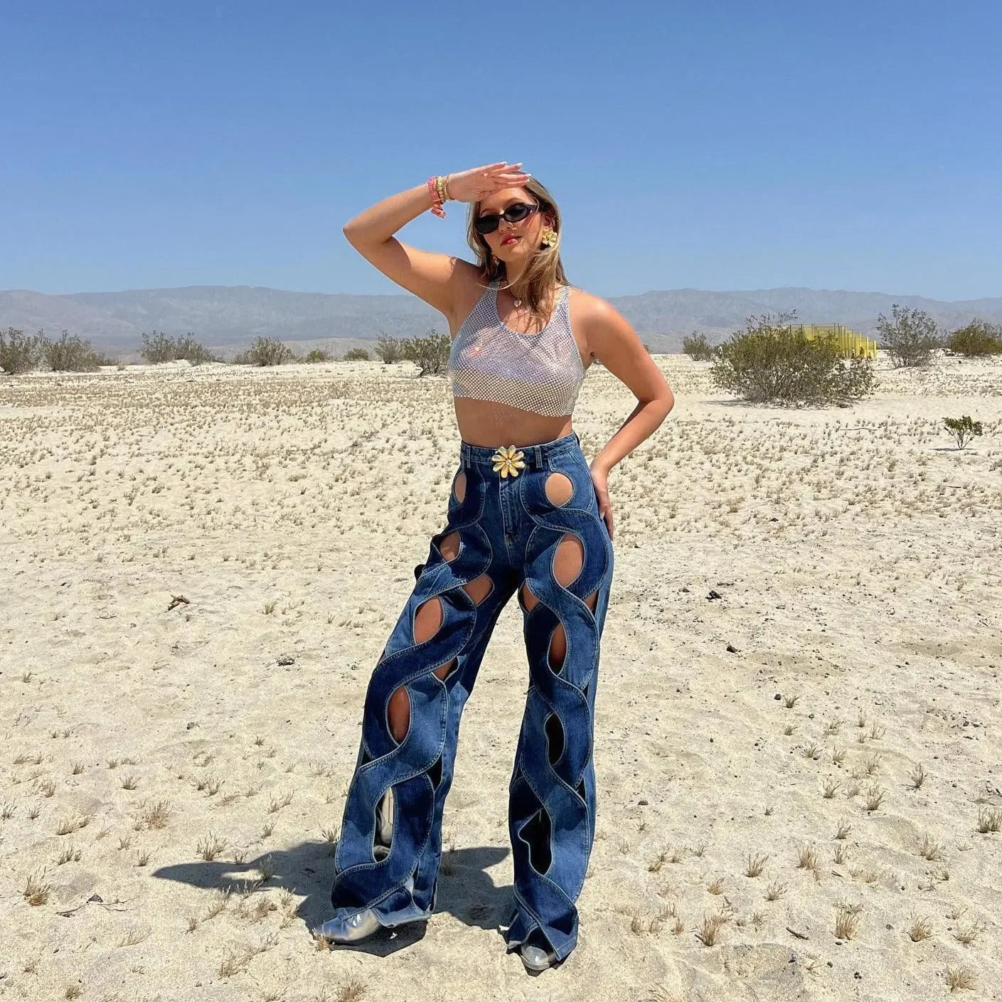 Silver mesh crop top paired with cut-out denim pants, edgy desert style.
