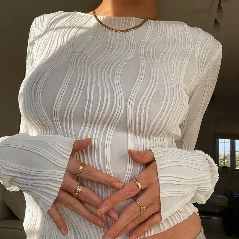 Textured white long-sleeve top with statement rings, elegant casual wear.