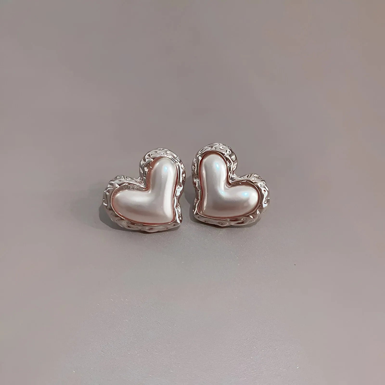 Heart-shaped pearl stud earrings with silver trim, elegant accessory.