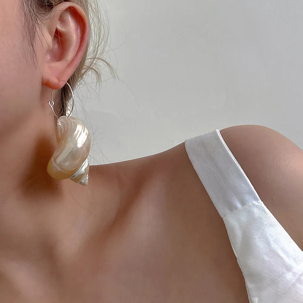 Shell-inspired statement earring with single strap satin detail, unique accessory styling.