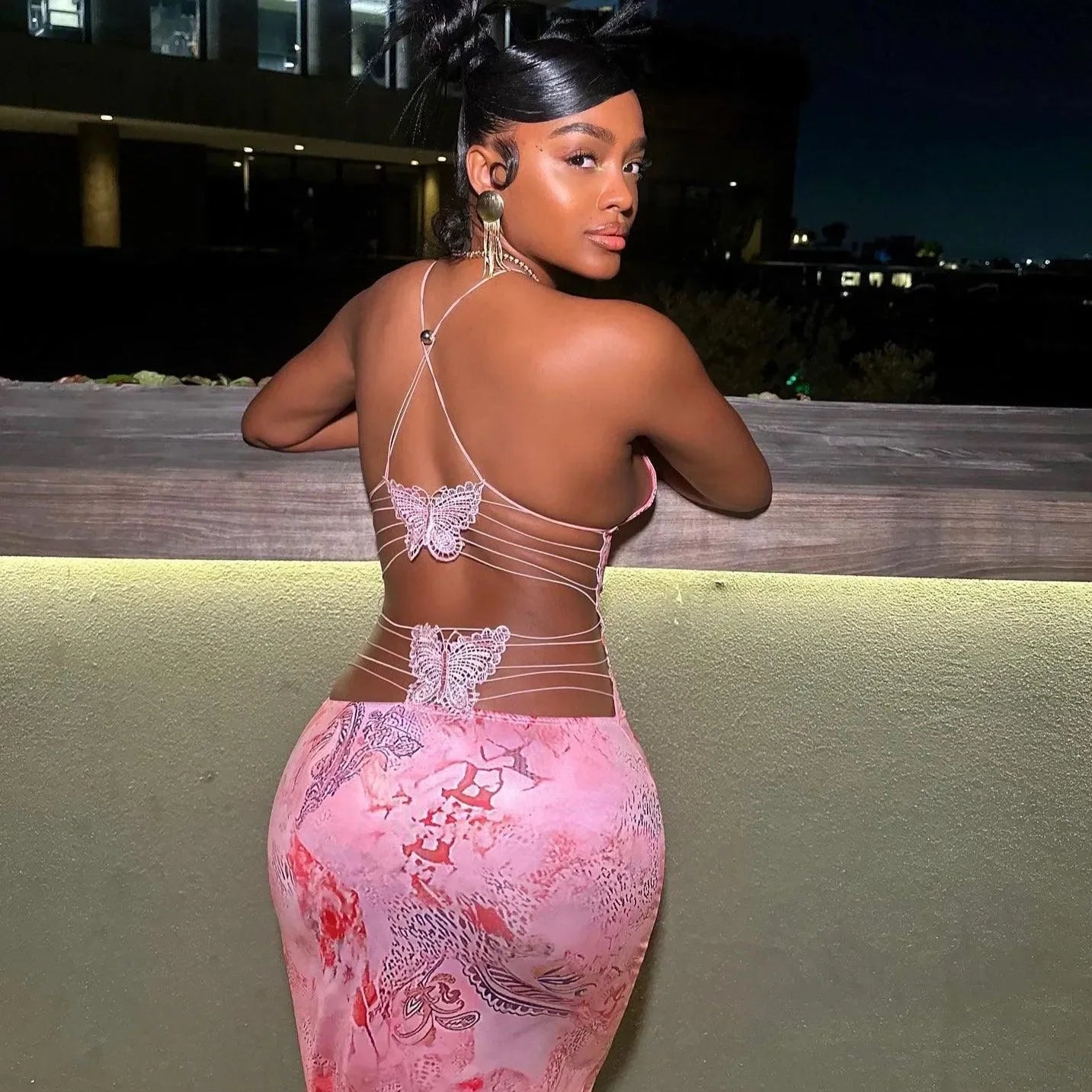 Backless pink maxi dress with butterfly lace details, night-out styling.