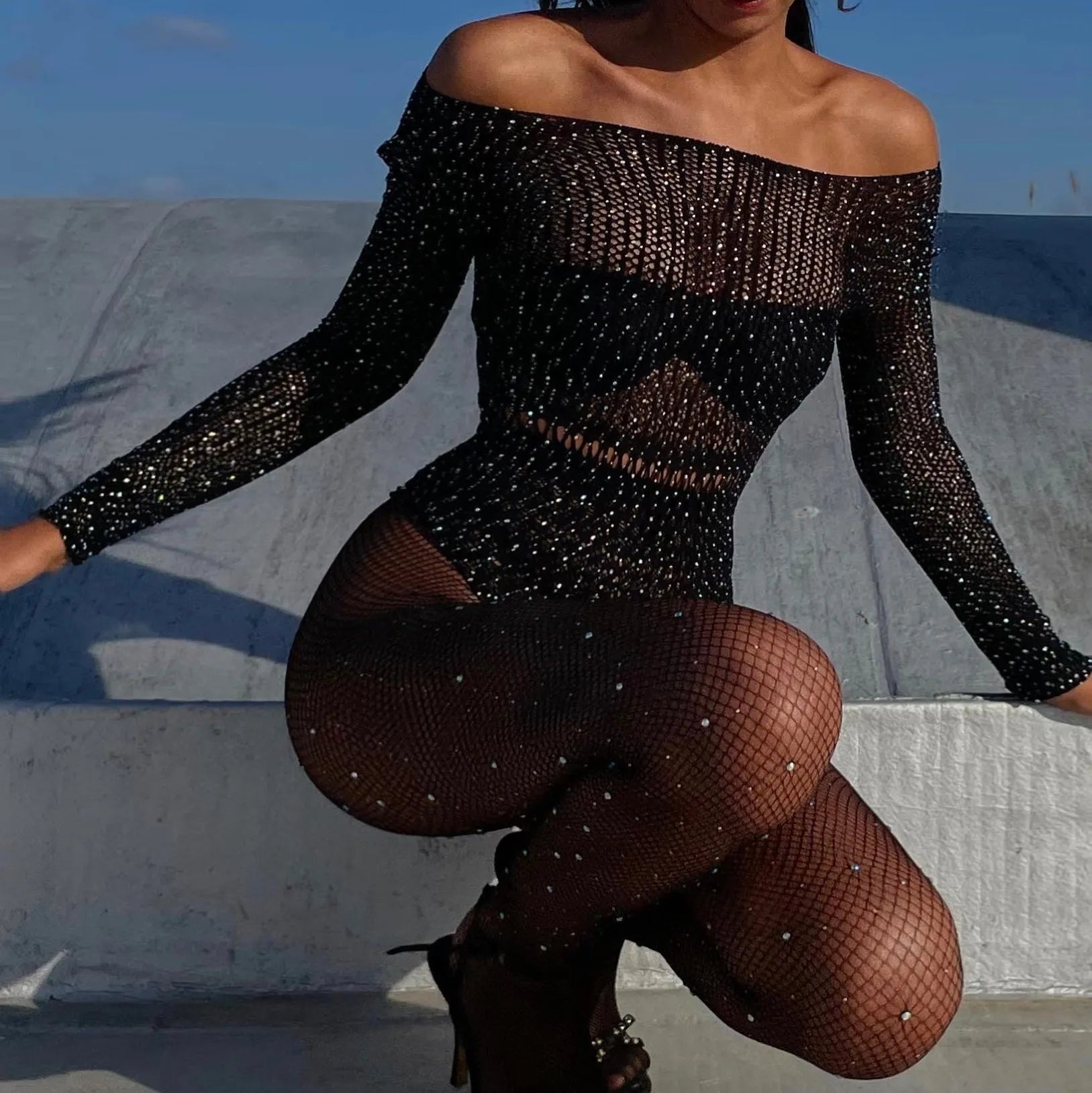 Black mesh bodysuit with diamond details, backless design, off-the-shoulder neckline, styled with high heels.