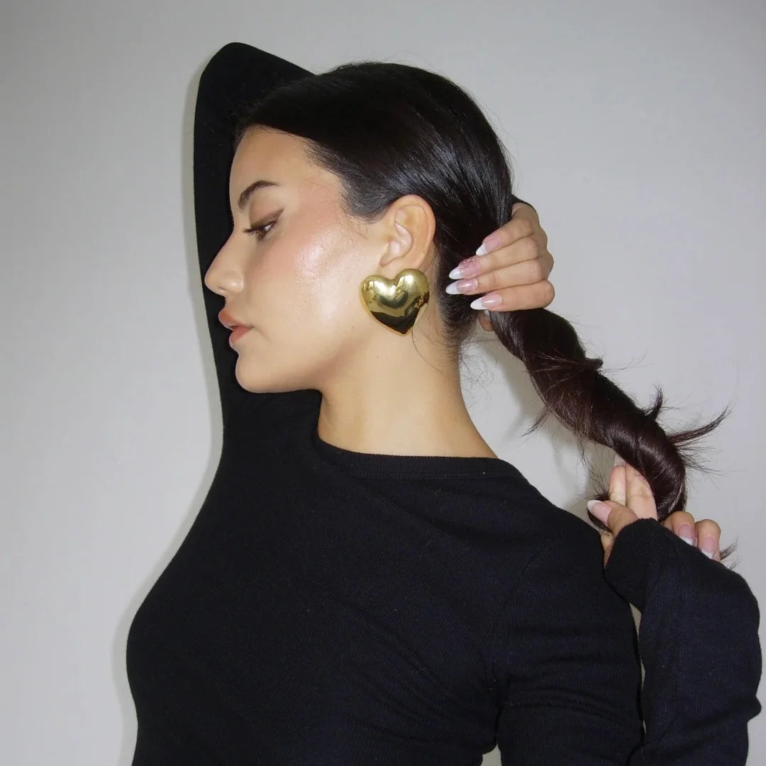 Long-sleeve black top with large gold heart-shaped earrings, chic and minimal accessory styling.