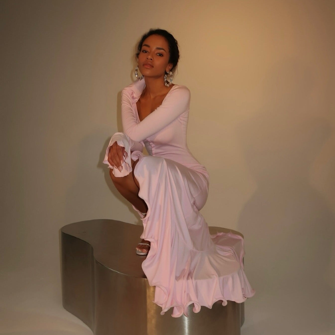 Pink ruffled midi dress featuring long sleeves and a fitted silhouette, styled with elegant heels for a chic look.