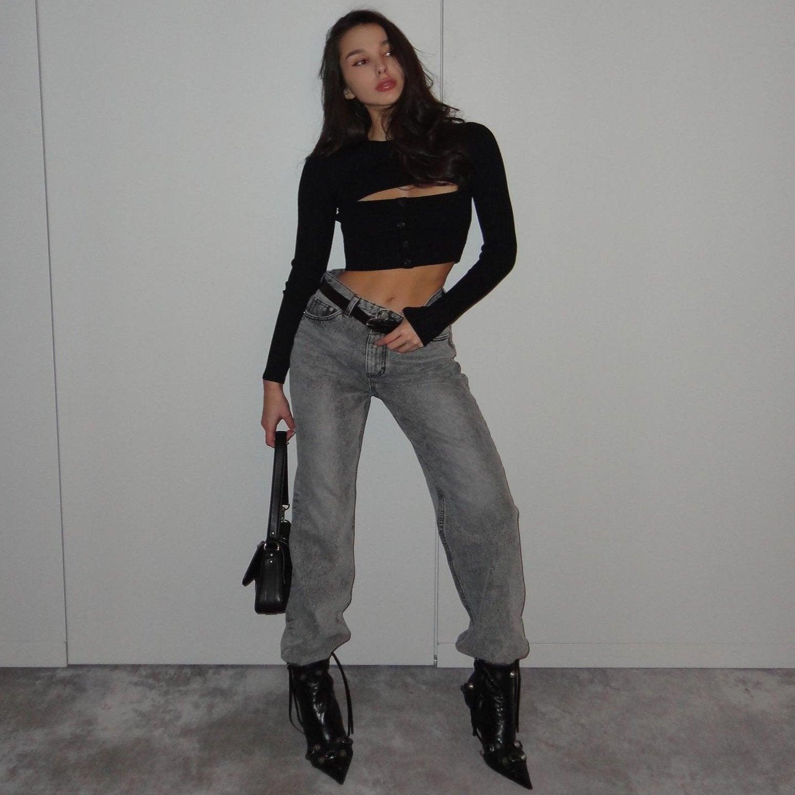 Black long sleeve ribbed top featuring a cutout detail, styled with high-waisted denim and pointed toe heels.