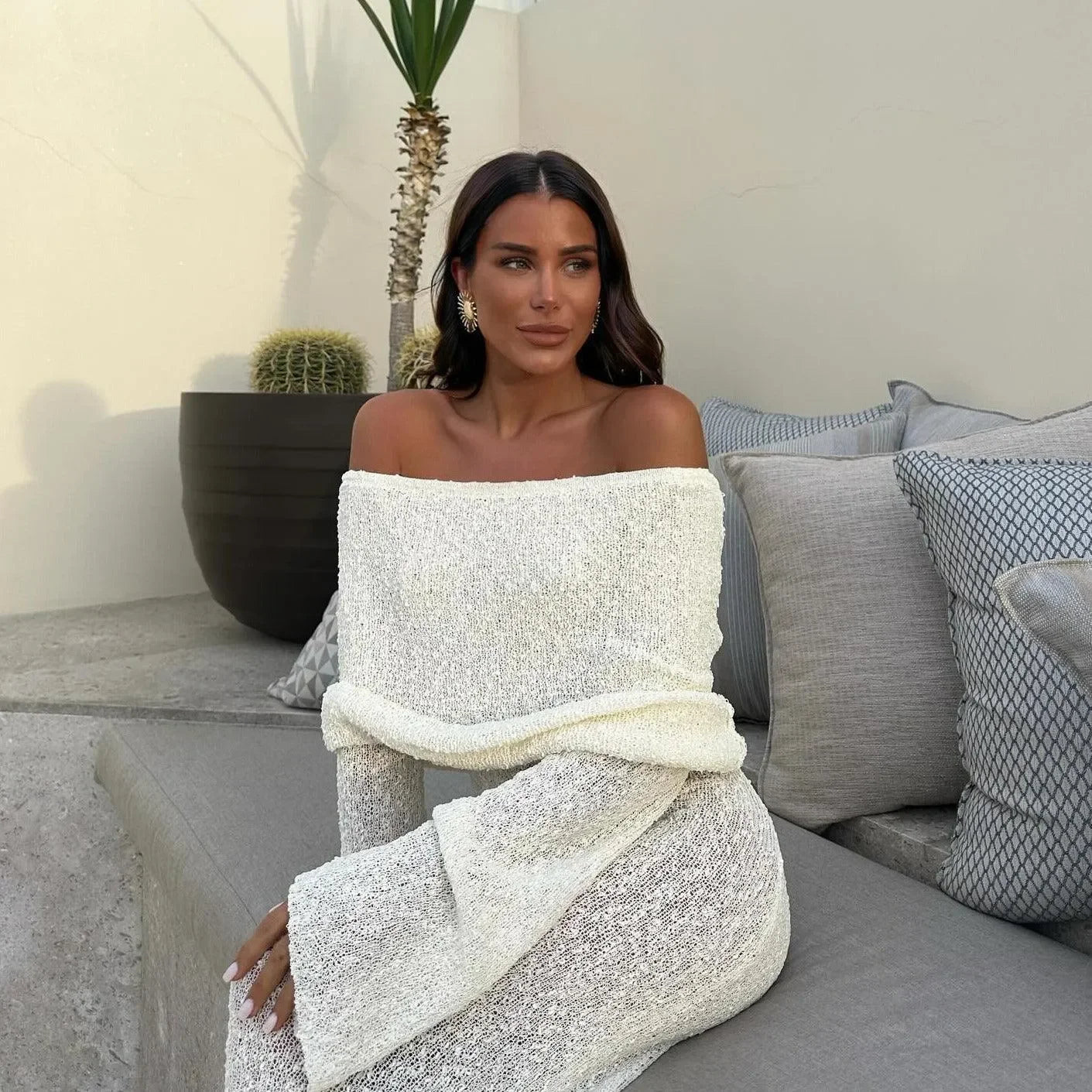 Off-shoulder white maxi dress with long sleeves, styled elegantly for a chic summer look. Perfect for outdoor gatherings.