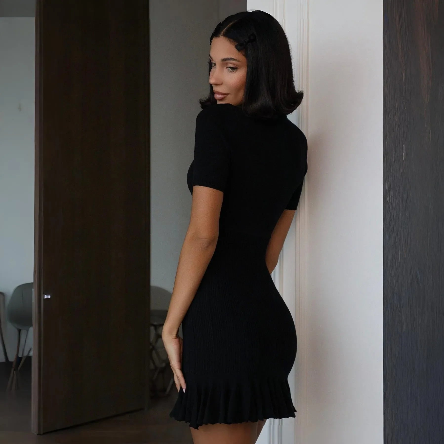 Black ruffled knit mini dress with short sleeves, fitted silhouette, styled for a chic, casual look.