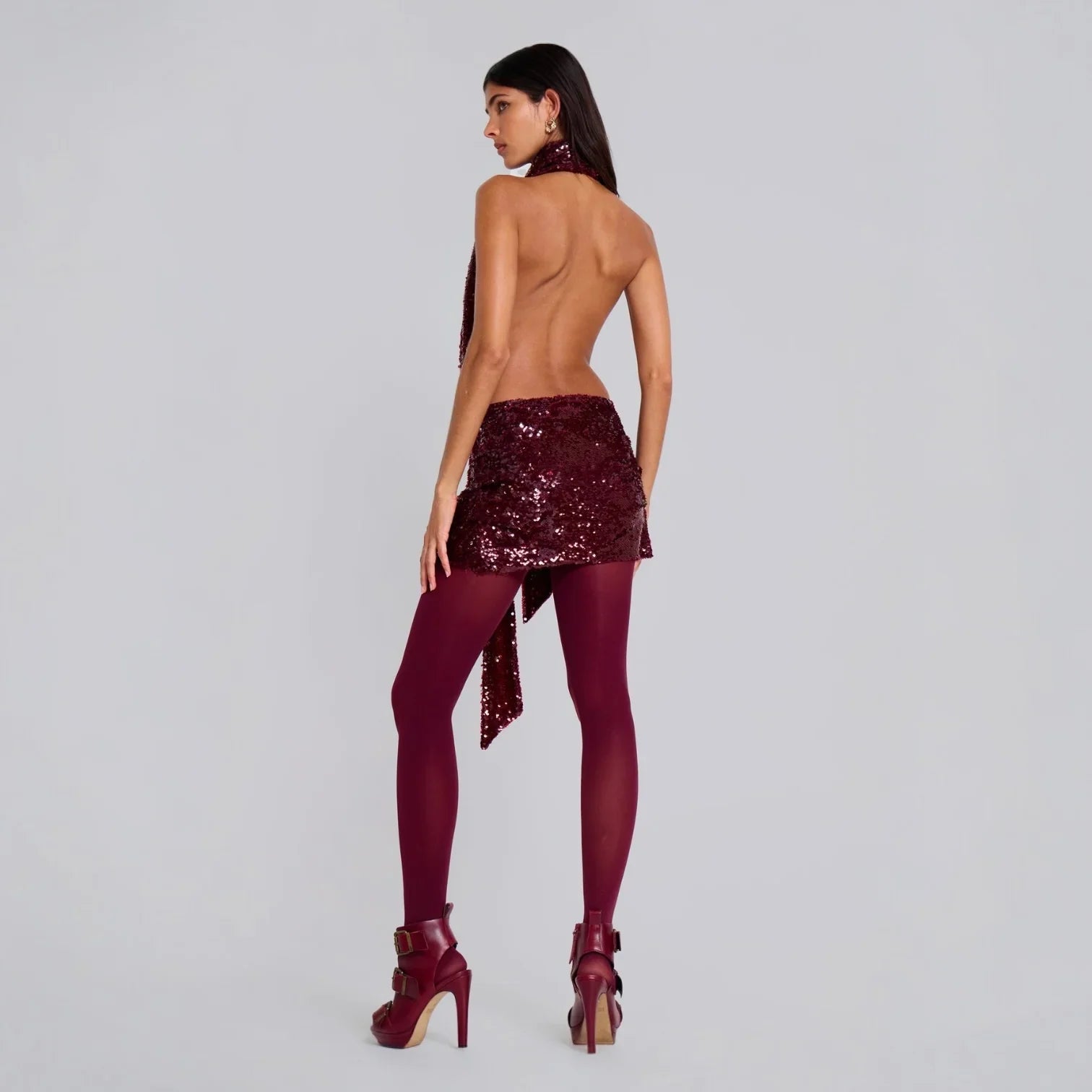 Backless burgundy sequin halterneck mini dress, styled with tights and high heels for a chic evening look.