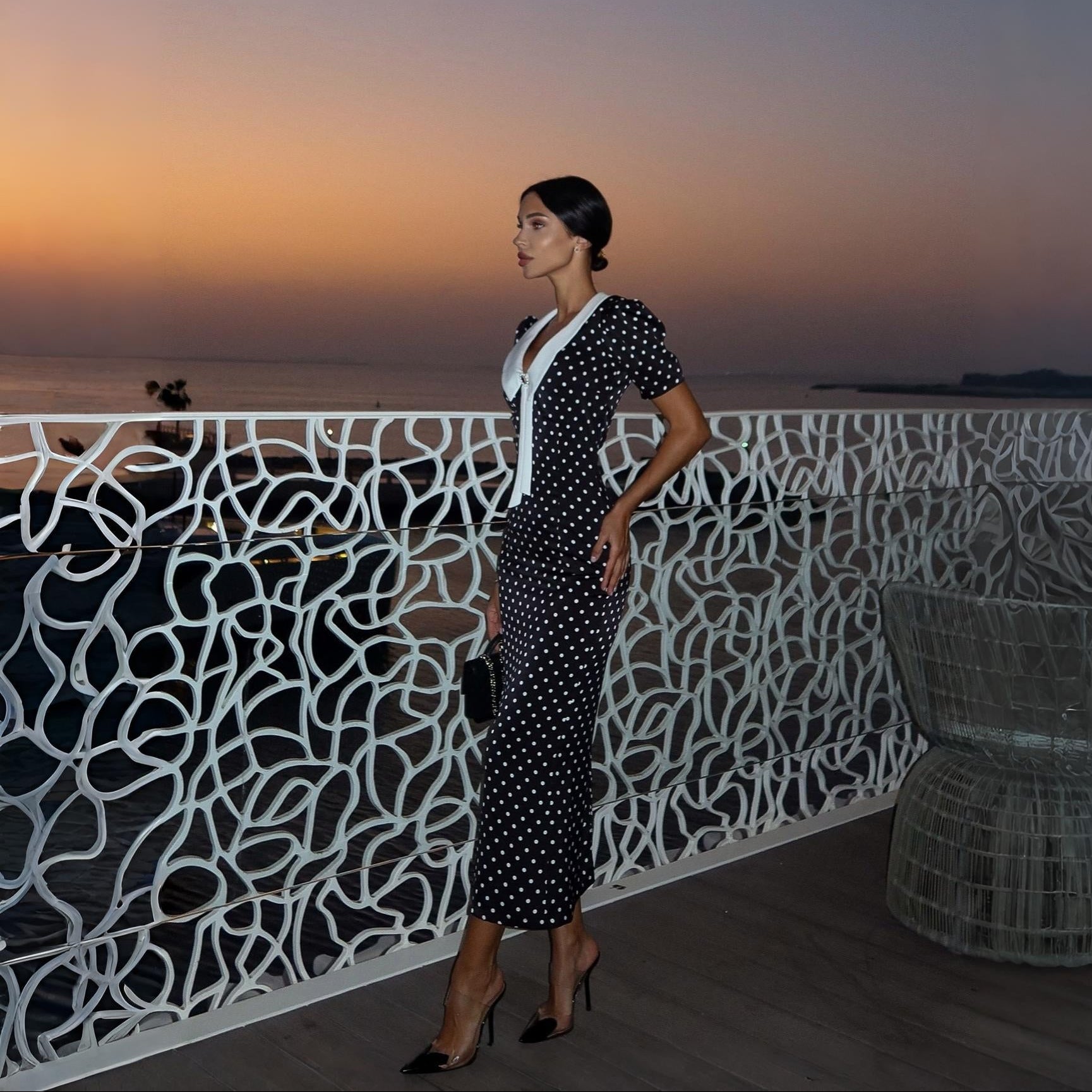 Black polka dot midi dress with puff sleeves and fitted waist, styled with elegant heels for a chic evening look.