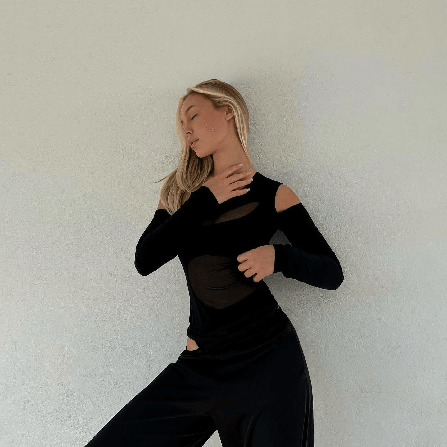 Black asymmetric sheer panel bodysuit with long sleeves, styled with relaxed trousers for an edgy yet elegant look.