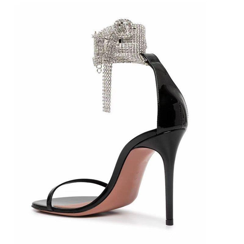 Black strappy high-heeled sandals with a sparkling diamond chain detail, ideal for dressing up evening outfits.