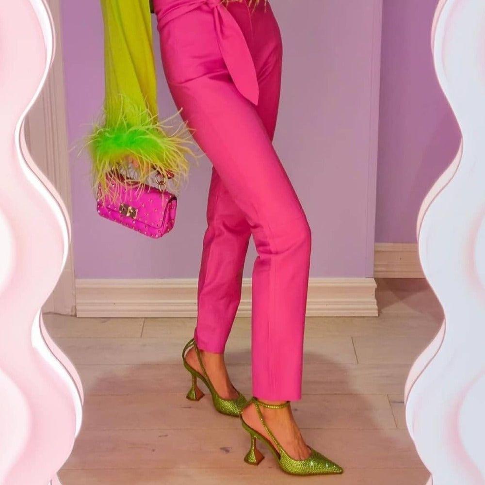 High shine green crystal lace-up heels paired with pink fitted trousers and a vibrant green feathered top.