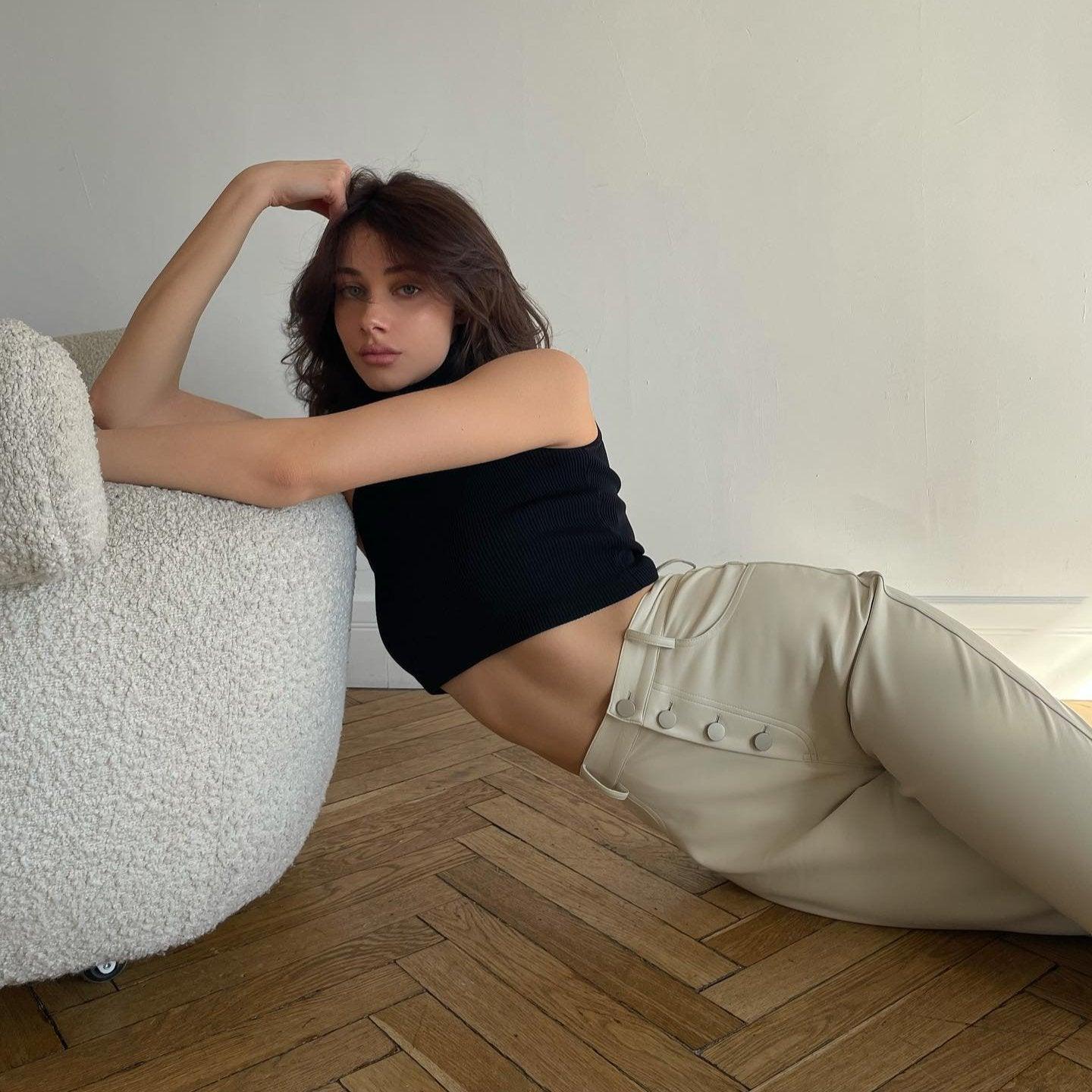 High-waist white leather pants with button details, styled with a black cropped top, perfect for chic casual looks.
