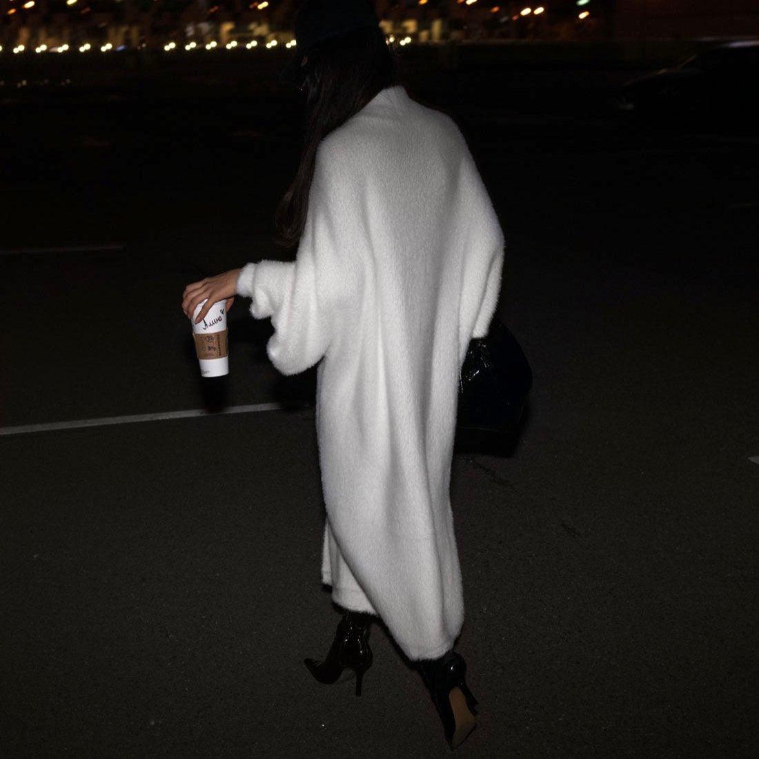 Oversized long sleeve cardigan in misty white, cozy texture, styled over fitted pants, carrying a coffee cup.