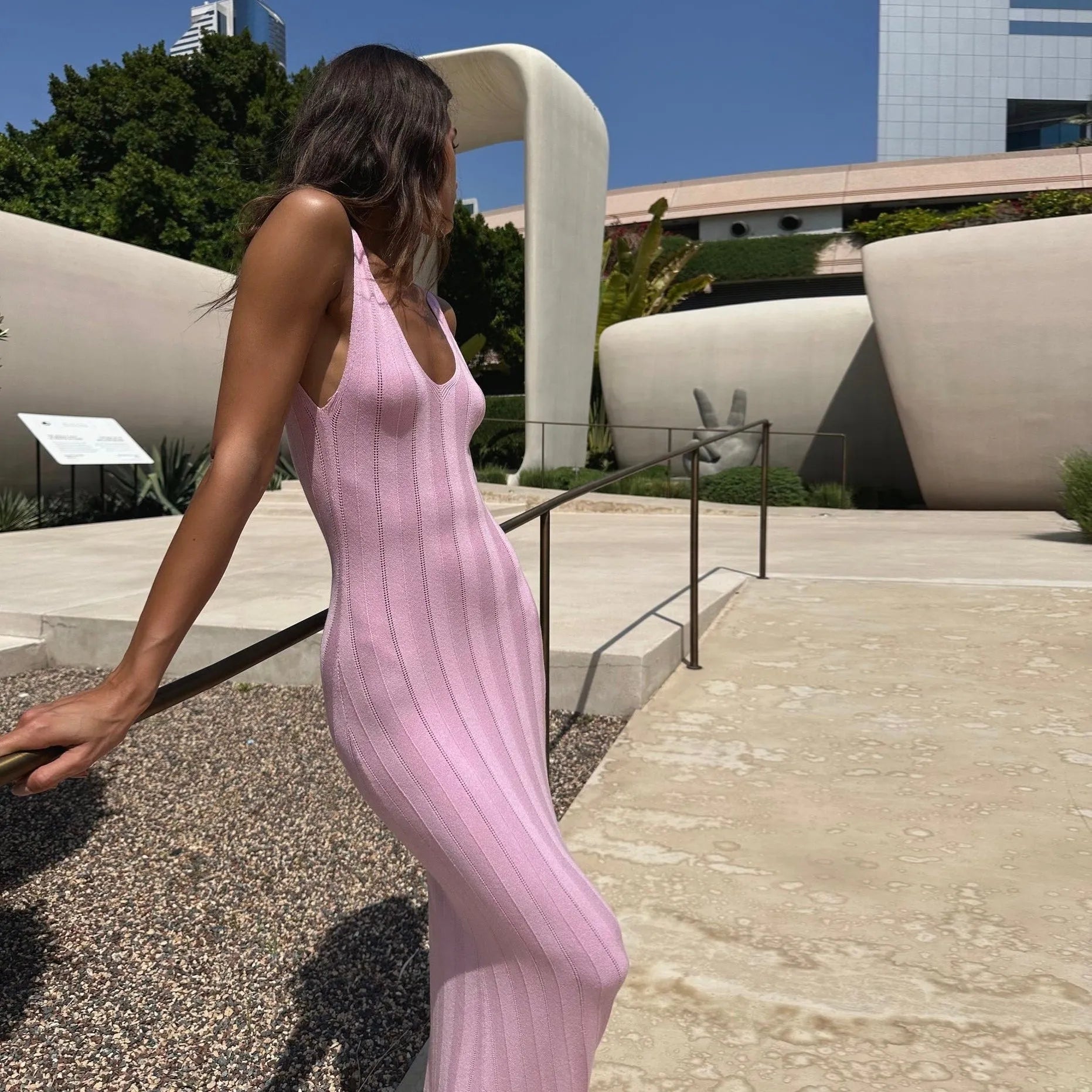 Backless pink knitted maxi dress with sleek vertical stripes, styled for a chic summer look. Perfect for an elegant outing.