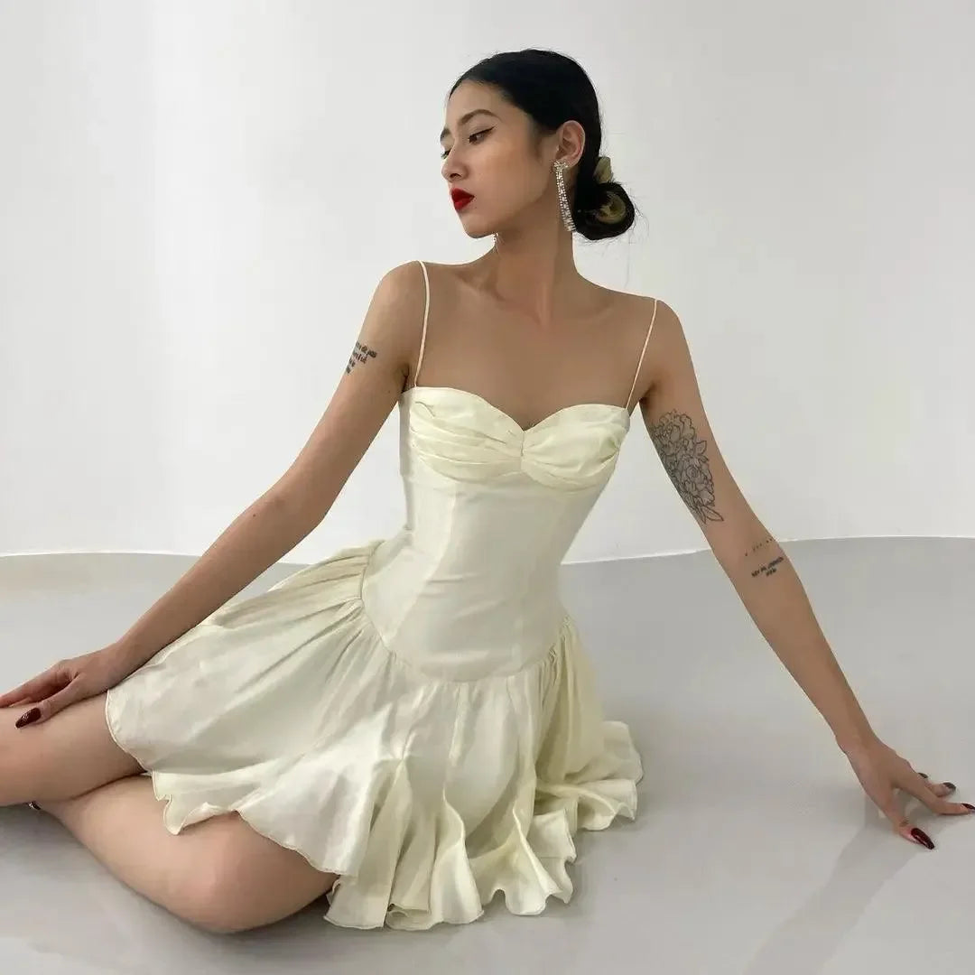Ivory mini dress with a sweetheart neckline, thin straps, and flared skirt, styled gracefully on a seated model.